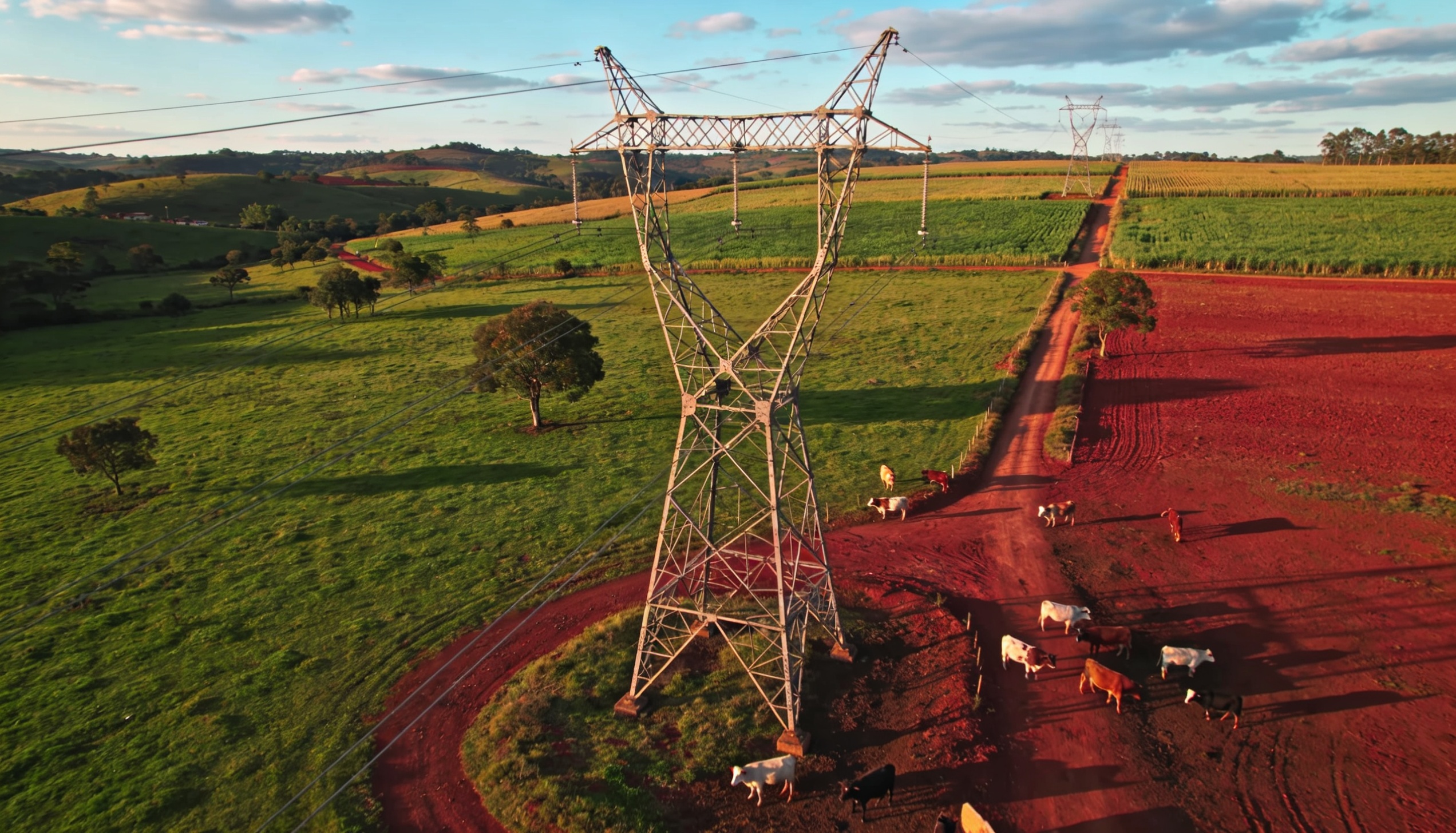 Vista aérea de propriedade rural com torre de transmissão mostrando as diferentes zonas de impacto — solo, pastagem, culturas e infraestrutura